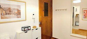 Ein Flur mit einem gerahmten Gemälde, einer Holztür, einem weißen Schrank mit einem Korb und einem an der Wand befestigten Telefon.