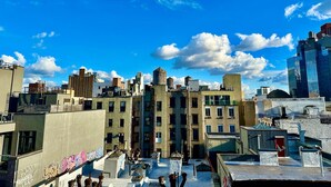A rooftop with a view of a cityscape, featuring buildings of various architectural styles and a clear blue sky with clouds. - Luxury in Little Italy 2 Bedroom - Private Balcony (New York)