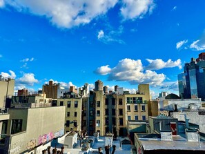 A rooftop with a view of a cityscape, featuring buildings of various architectural styles and a clear blue sky with clouds. - Luxury in Little Italy 2 Bedroom - Private Balcony (New York)