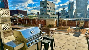 An outdoor patio with a barbecue grill, seating area, and a cityscape view in the background. - Luxury in Little Italy 2 Bedroom - Private Balcony (New York)