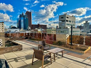A rooftop terrace with outdoor seating, a city skyline in the background, and a clear sky. - Luxury in Little Italy 2 Bedroom - Private Balcony (New York)