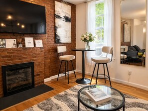A modern living room with a brick fireplace, a flat-screen TV, and a large abstract painting. - Beauty In the Heart of the Village (New York)