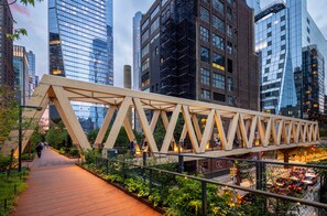 A pedestrian bridge with a wooden truss design over a pathway with greenery and urban buildings in the background. - West Village Wonder - Amazing Location (New York)