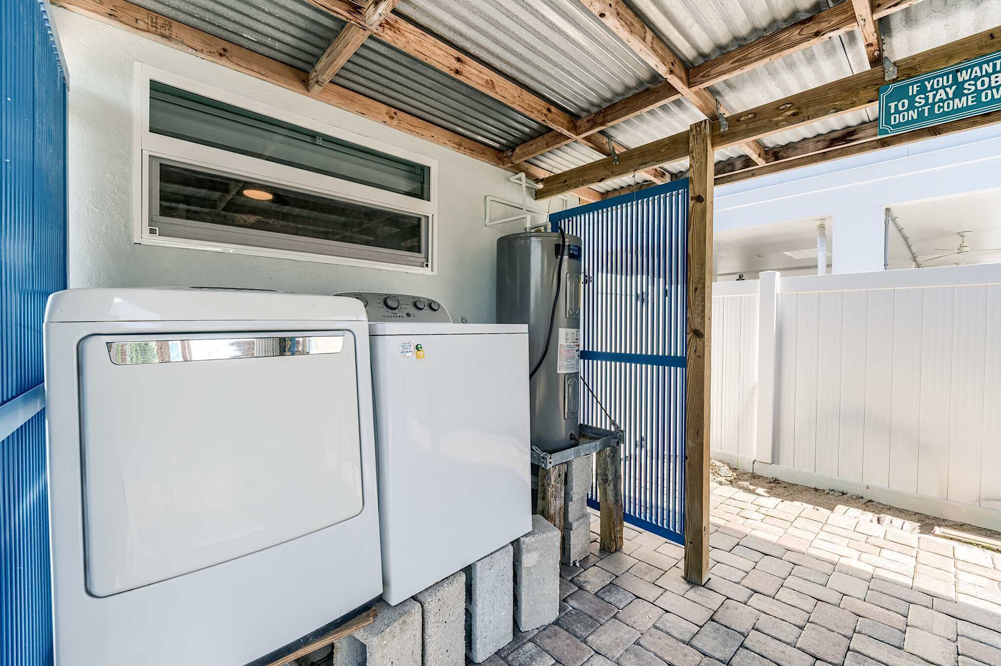 A laundry area with two washing machines, a water heater, and a blue gate.