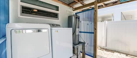 A laundry area with two washing machines, a water heater, and a blue gate.
