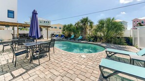 A swimming pool with lounge chairs and a table, surrounded by potted plants and a clear sky. - Sunshine Nook - 1/2 Block to the Beach (Fort Myers Beach)