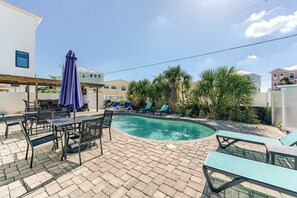 A swimming pool with lounge chairs and a table, surrounded by potted plants and a clear sky. - Sunshine Nook - 1/2 Block to the Beach (Fort Myers Beach)