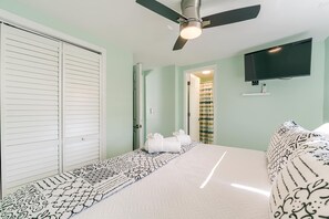 Ein Schlafzimmer mit einem Bett, einem Deckenventilator, einem Fernseher und einer Tür zu einem Badezimmer.