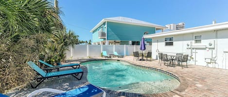 A swimming pool with lounge chairs, a patio area, and a house with a white exterior.