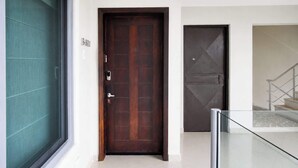 Um corredor com guarda-corpo de vidro, uma porta de madeira e uma porta escura.