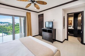 Ein Hotelzimmer mit einem Bett, einem Fernseher auf einer Kommode, einem Deckenventilator und Blick auf eine Stadtlandschaft durch große Fenster.