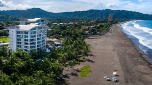 Hotel à beira-mar com vista para a praia, rodeado por palmeiras e montanhas ao fundo.