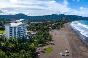 Ein Küstenhotel mit Blick auf den Strand, umgeben von Palmen und einem Bergpanorama.