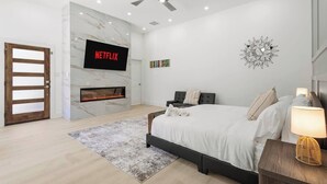 Ein modernes Schlafzimmer mit Kamin, einem Bett, einem an der Wand befestigten Fernseher und einem Deckenventilator.