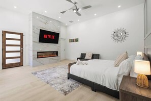 A modern bedroom with a fireplace, a bed, a TV mounted on the wall, and a ceiling fan. - Lux Home-Cinema+GamesGolf-Heated Pool-Hot Tub (Dallas)