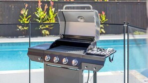 Ein Grill mit digitaler Anzeige in der Nähe eines Schwimmbeckens mit Metallzaun.