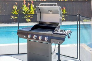 A barbecue grill with a digital display, positioned near a swimming pool with a metal fence. - Lux Home-Cinema+GamesGolf-Heated Pool-Hot Tub (Dallas)