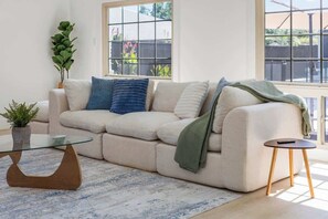 A living room with a sofa, a glass coffee table, a small side table, and a potted plant. - Lux Home-Cinema+GamesGolf-Heated Pool-Hot Tub (Dallas)