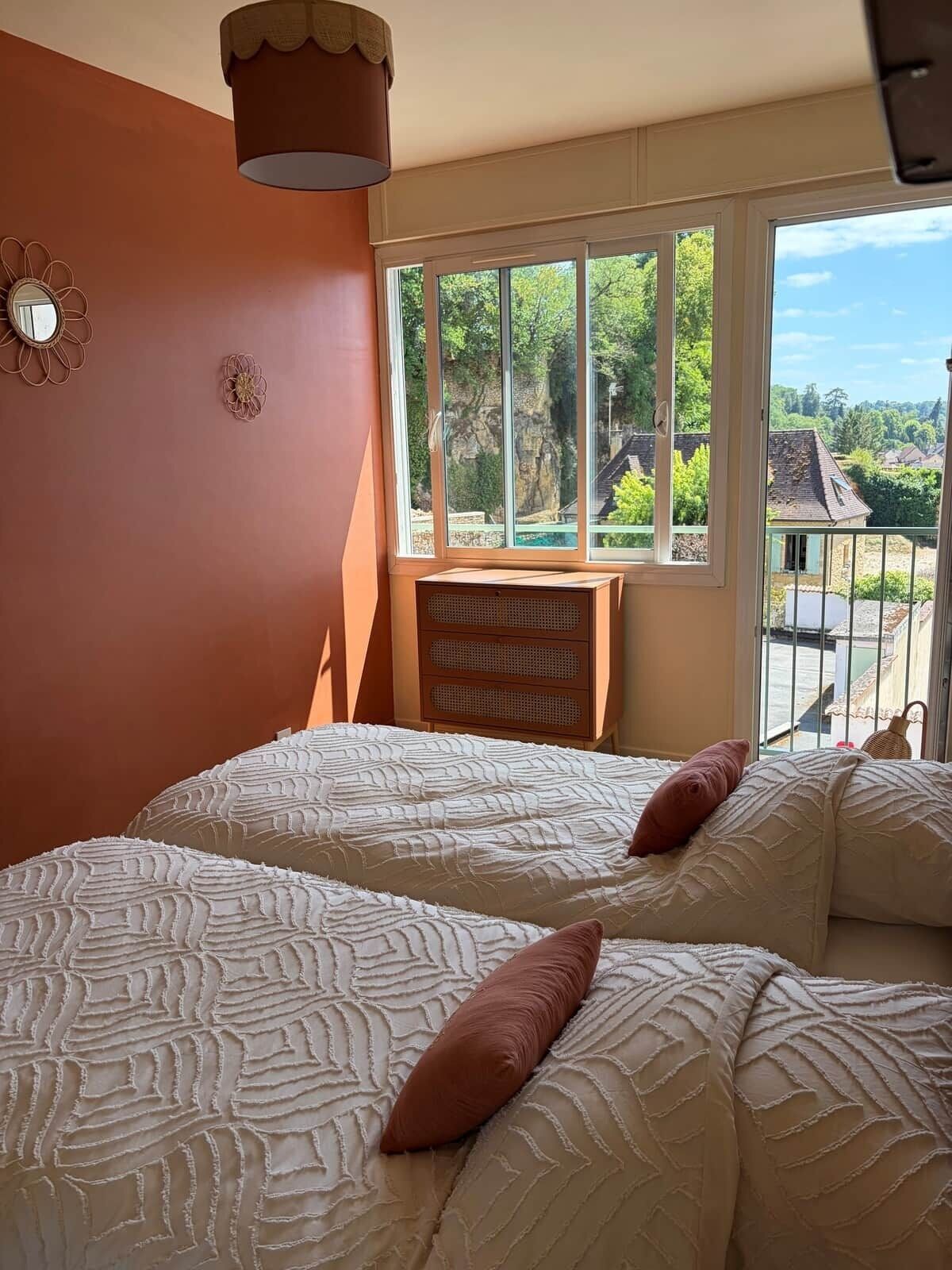 Un dormitorio con dos camas, una ventana que da a zonas verdes y una lámpara en el techo.
