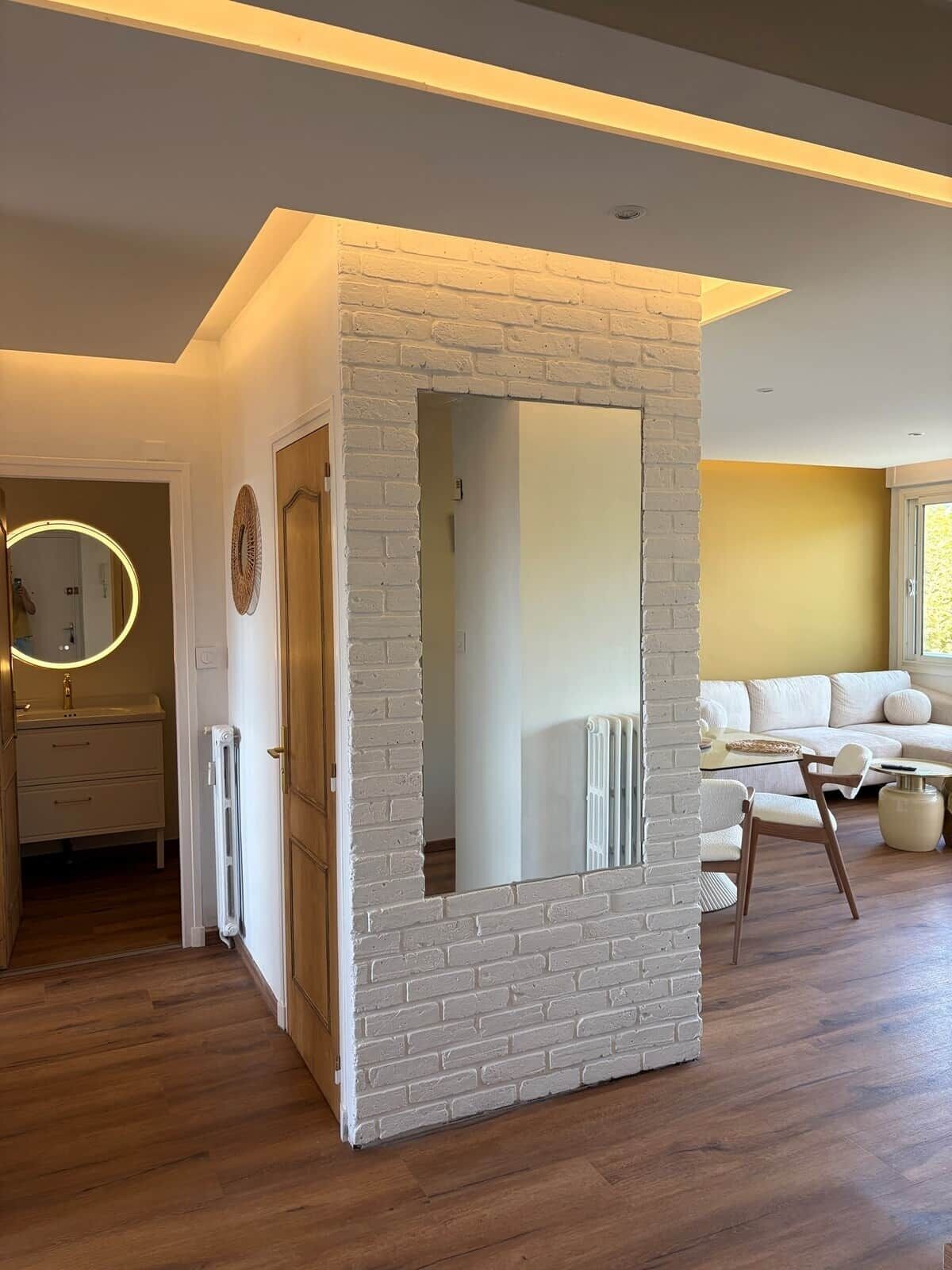Een moderne woonkamer met een accentmuur van witte baksteen, een ronde spiegel, een bank en een salontafel.