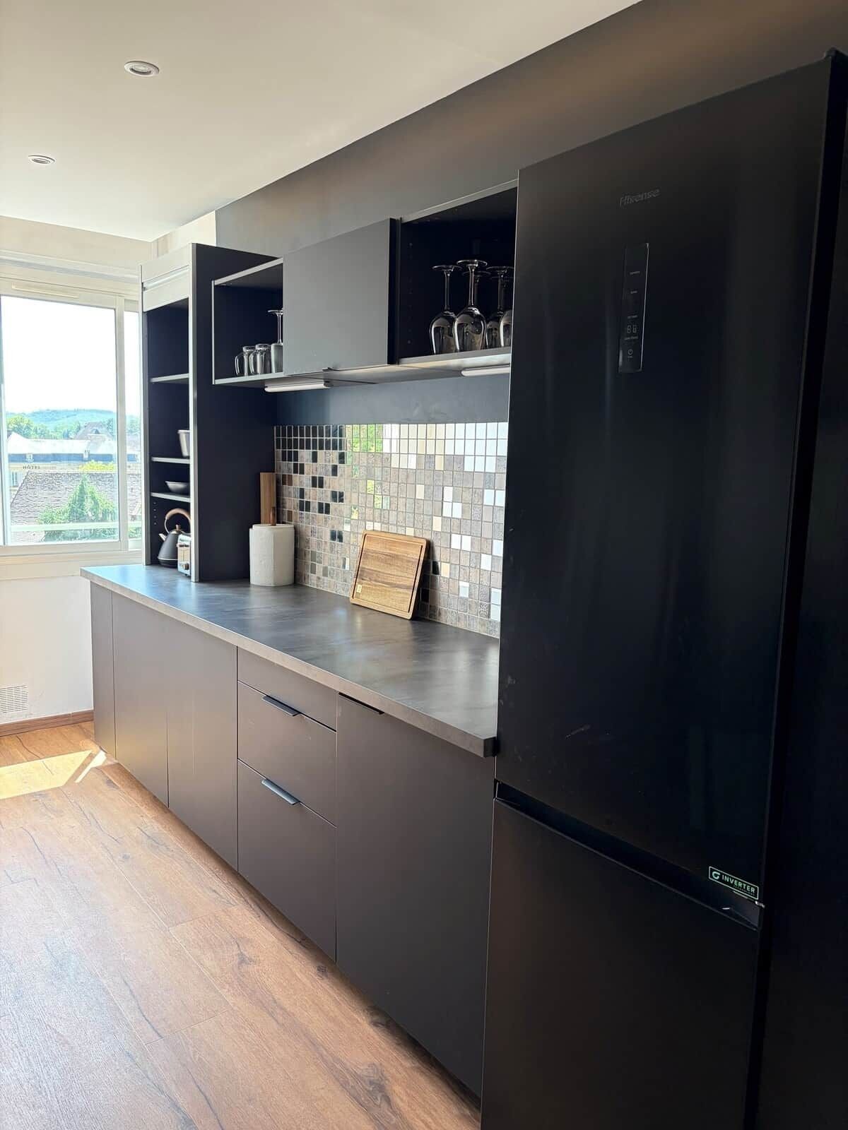 Une cuisine moderne avec un réfrigérateur noir, un plan de travail en bois et une vue par la fenêtre.