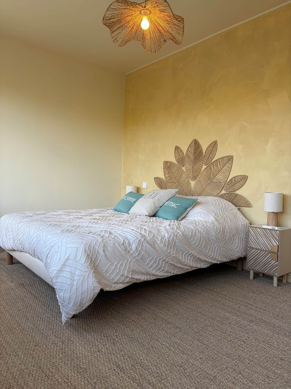 Une chambre avec un grand lit, une décoration murale en forme de feuille, une lampe de chevet et une moquette à motifs.