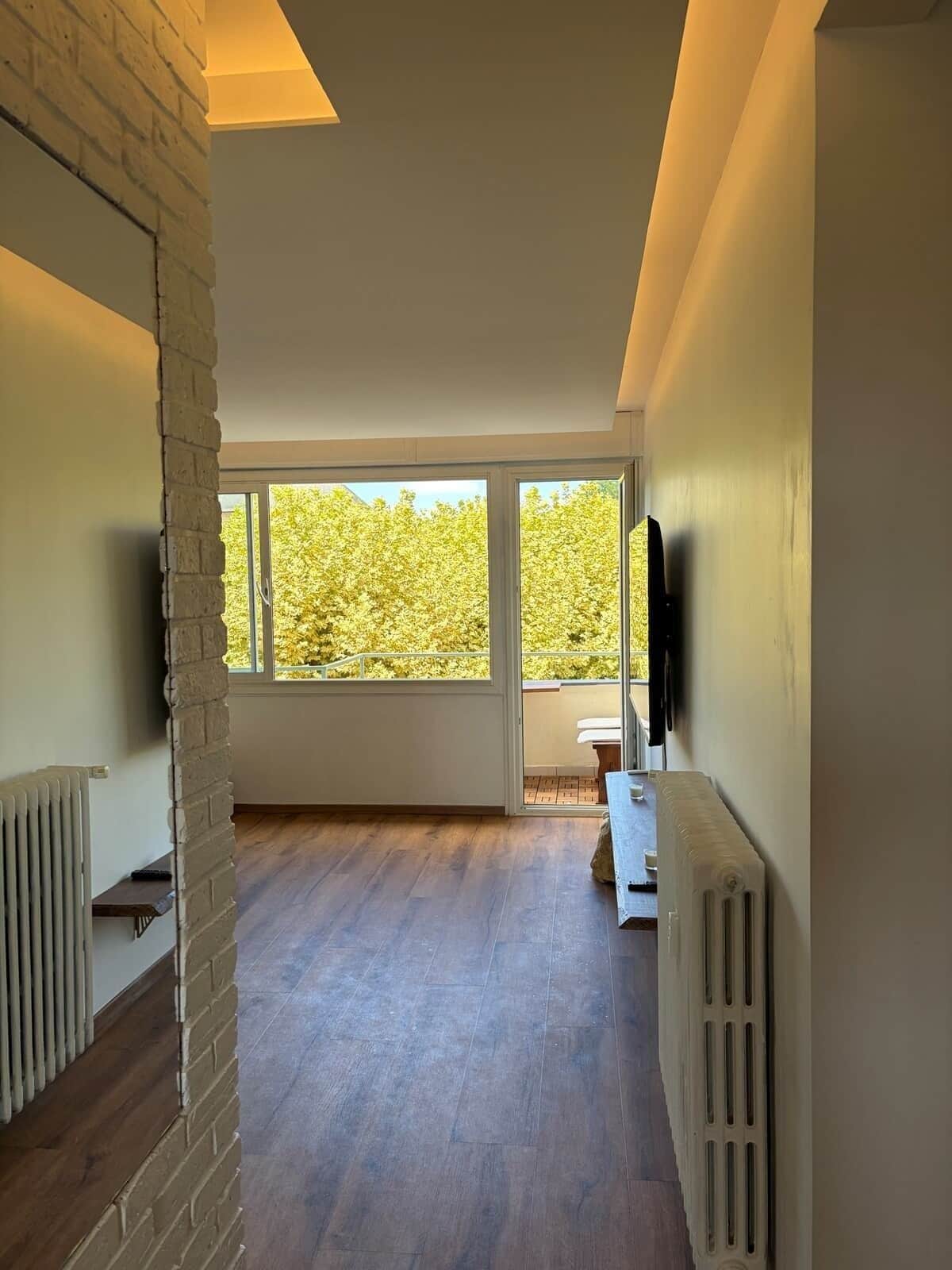 Une pièce spacieuse avec une grande fenêtre, un plancher en bois et un mur en briques.