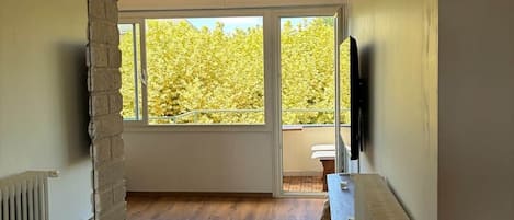 Una habitación amplia con un ventanal grande, piso de madera y pared de ladrillo.