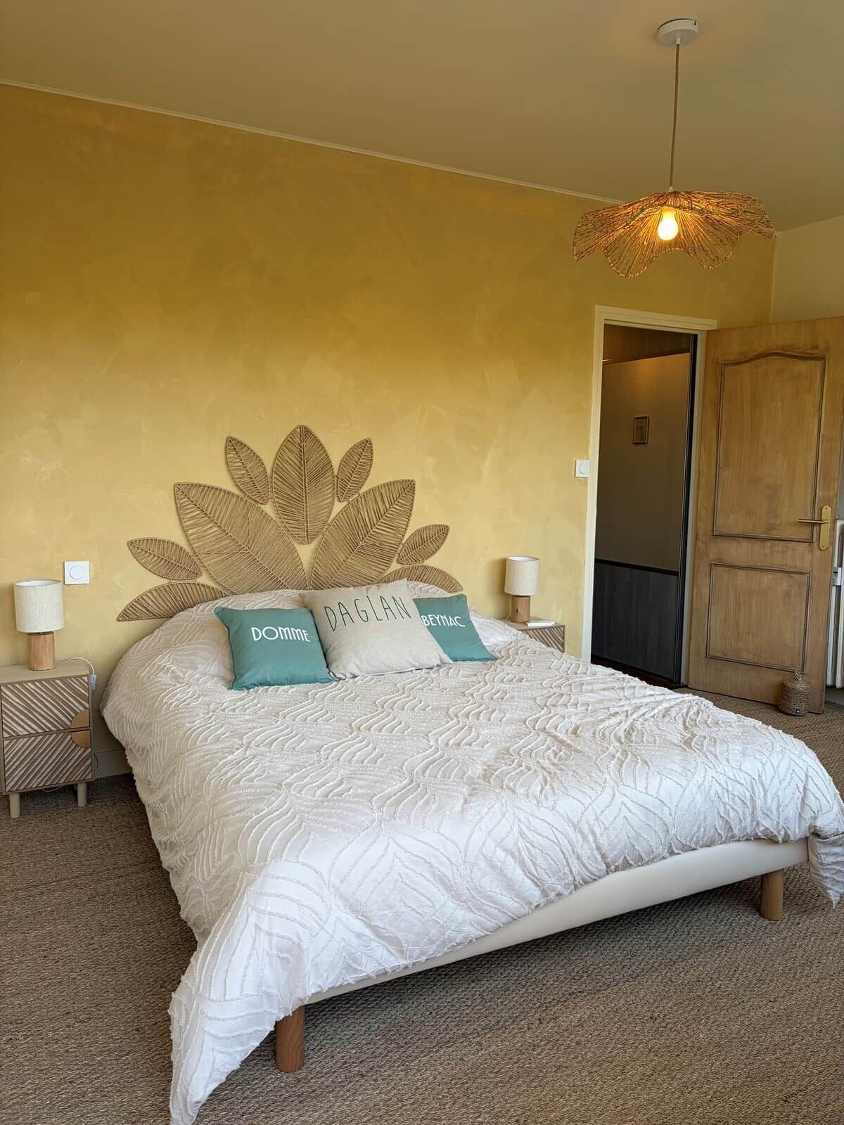 Un dormitorio con una cama grande, dos lámparas de noche, una lámpara de pared y una puerta a otra habitación.