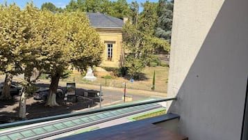 A balcony with a table and seating, overlooking a courtyard with trees and a building.