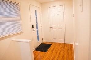 A hallway with a wooden floor, a black doormat, and a white door with a window. - Cozy 2-bedroom house in charming Niles with AC (Niles)