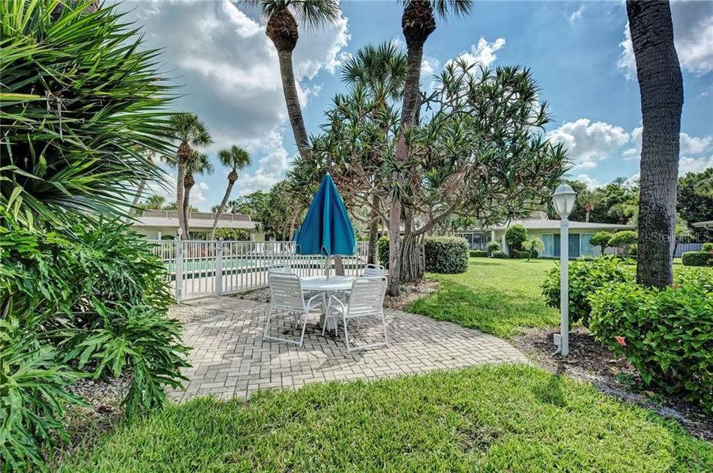 A patio area with a table and chairs, surrounded by palm trees and a white fence.