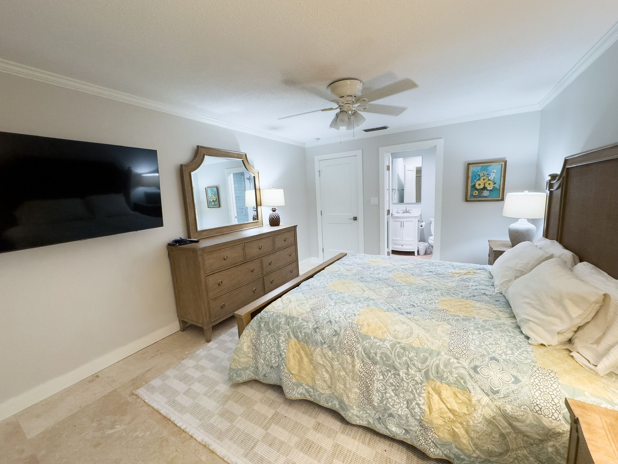 Une chambre à coucher comprenant un lit, une commode, un ventilateur de plafond et un téléviseur fixé au mur.