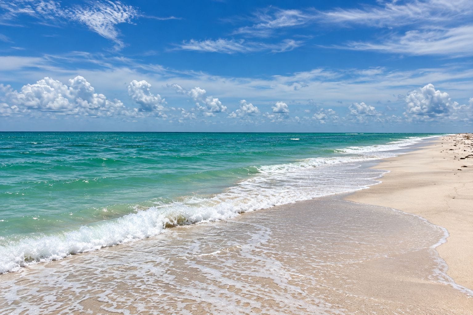 Een strand met helder turquoise water, zachte golven en een zandstrand.