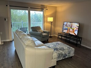 A living room with a sofa, armchair, ottoman, TV, and a lamp.