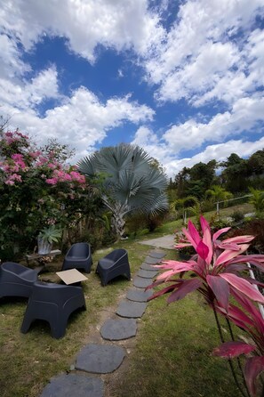 A garden with a stone pathway, outdoor seating, and various plants.