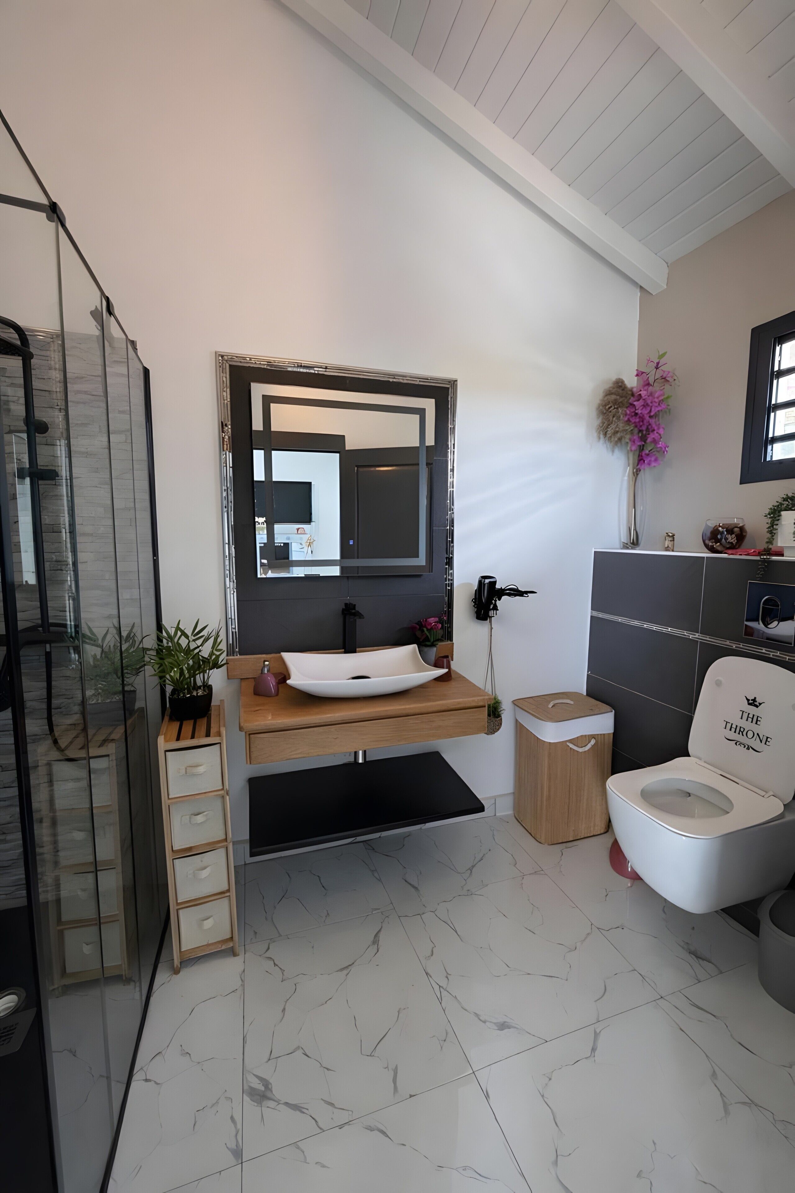 Une salle de bain moderne avec un grand miroir, un lavabo blanc, des toilettes et un espace douche.