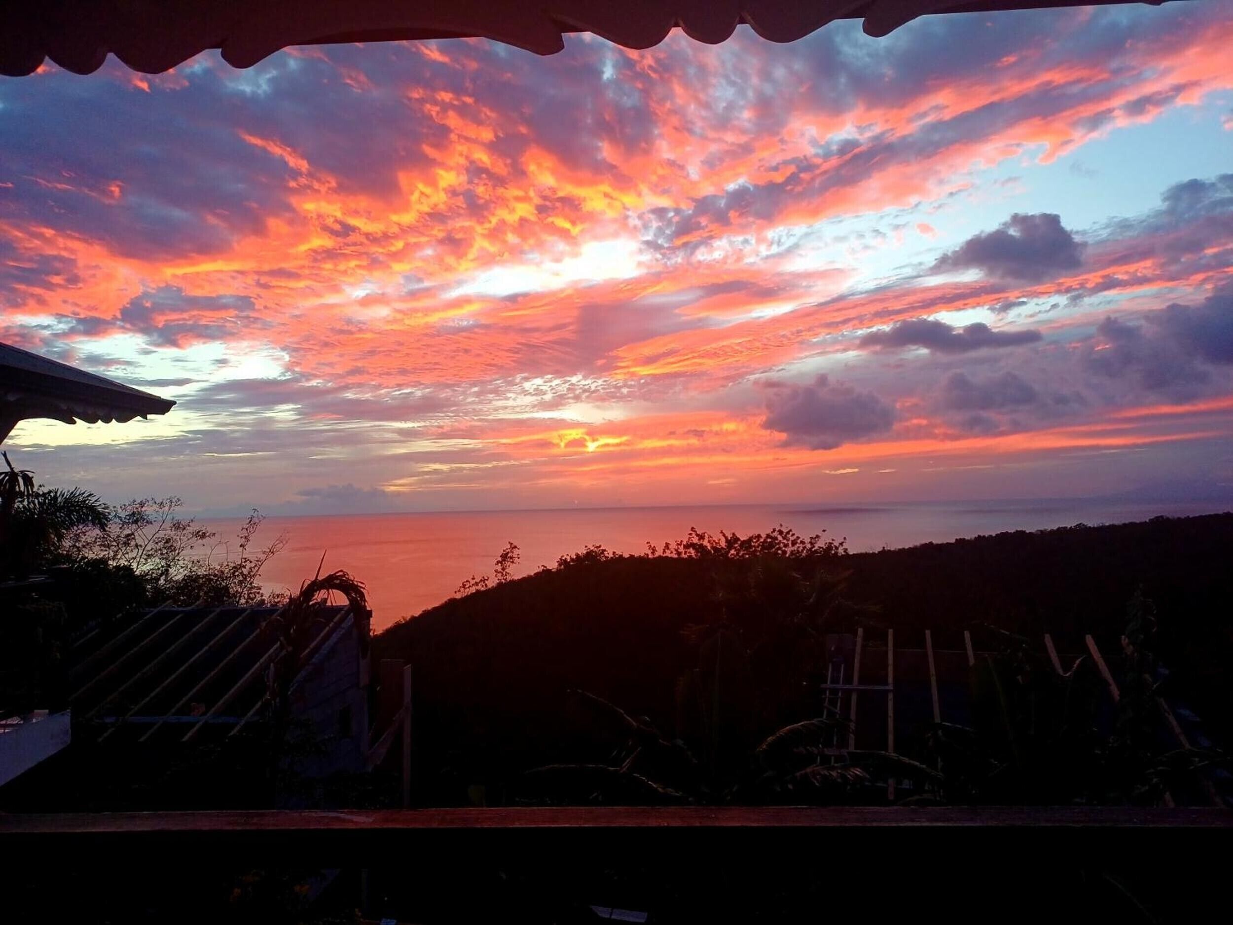 Un coucher de soleil avec vue sur la mer et la silhouette d’un bâtiment coiffé d’un toit.