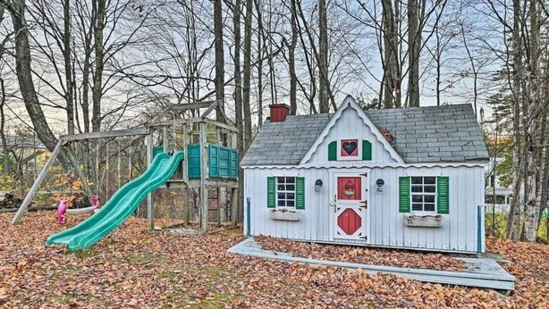 Ein Spielplatz mit einer Rutsche und einem hausähnlichen Bauwerk mit roter Tür und grünen Fensterläden.