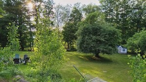 Ein grünes Außenbereich mit einer Hängematte, einer kleinen Gartenhütte und einer Gruppe von Adirondack-Stühlen.