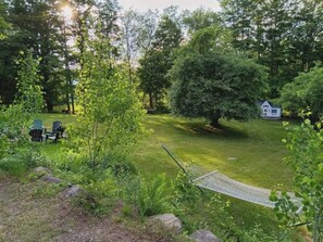 Ein grünes Außenbereich mit einer Hängematte, einer kleinen Gartenhütte und einer Gruppe von Adirondack-Stühlen.