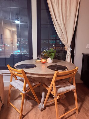 Une table de salle à manger ronde en bois, avec quatre chaises, une plante en pot et une bougie posée sur la table.