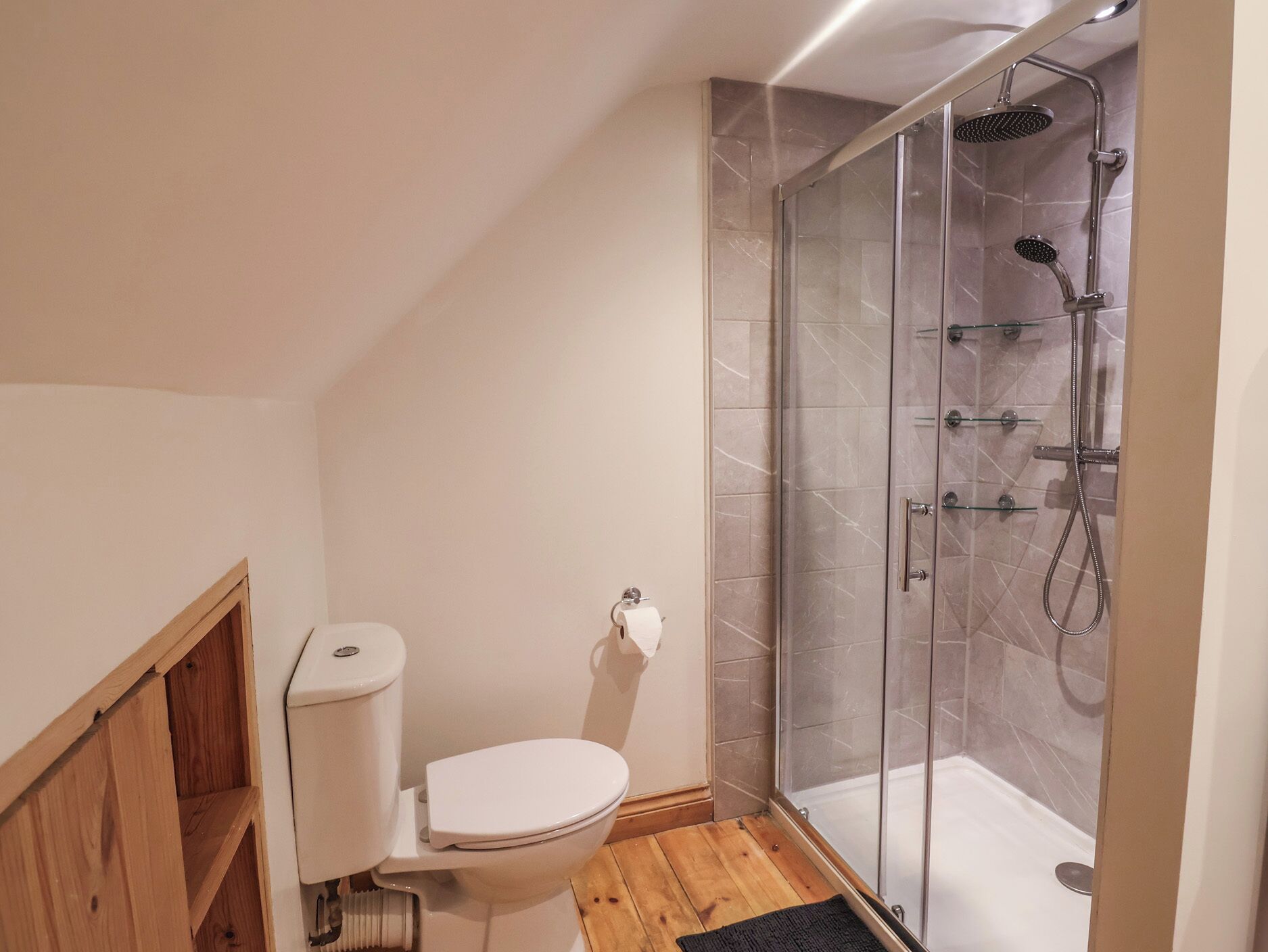 A bathroom with a toilet, a glass shower enclosure, and wooden flooring.