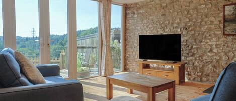 A living room with a stone wall, a flat-screen TV on a wooden stand, and a large sliding glass door leading to a deck.