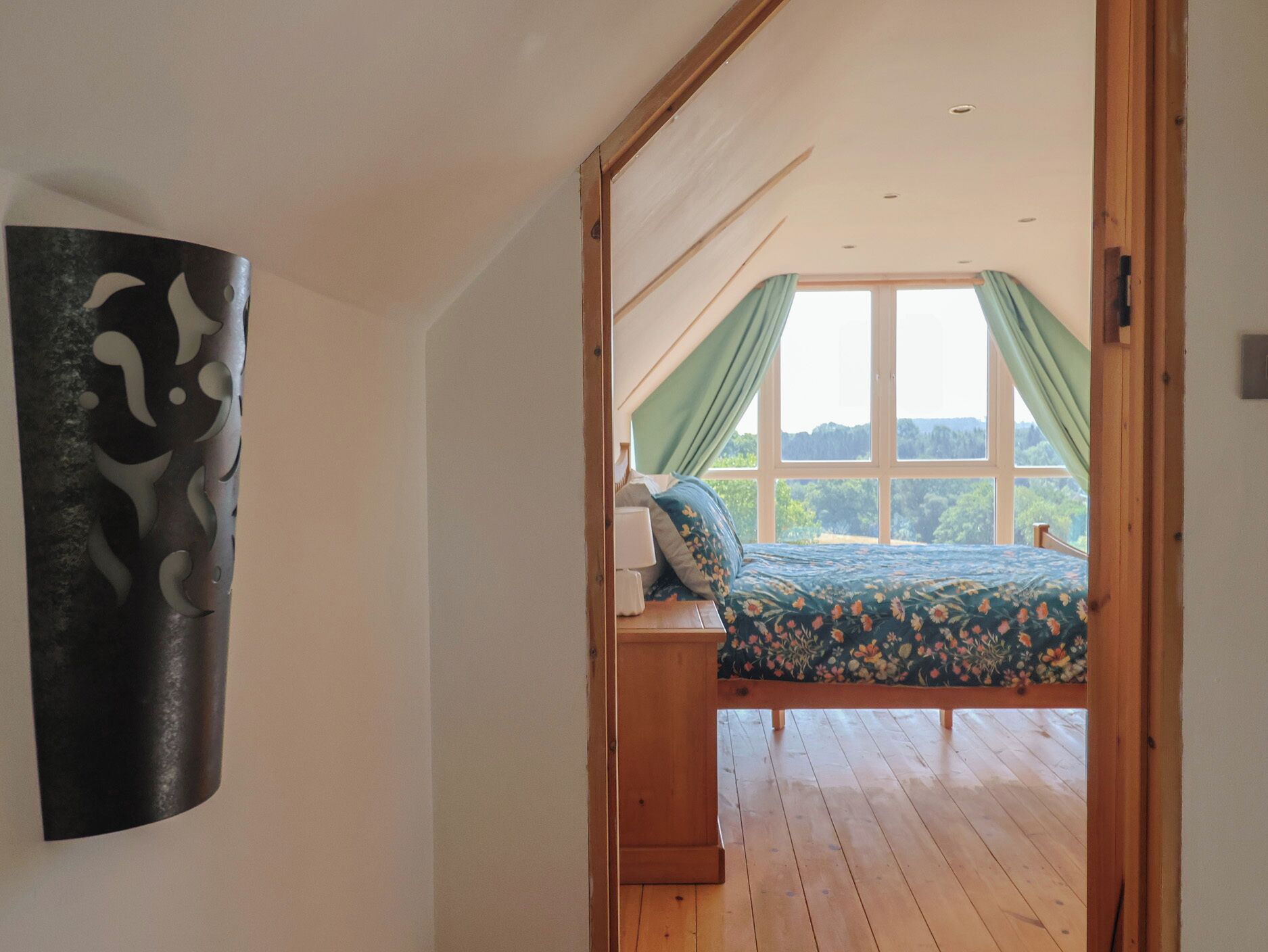 A bedroom with a wooden bed, a nightstand, and a large window with curtains.