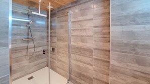 Un área de ducha moderna con puerta de cristal, techo de madera y paredes con azulejos.