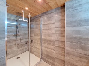 Ein modernes Duschbad mit Glastür, Holzboden und Fliesenwänden.
