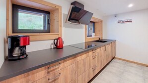 Cocina moderna con armarios de madera, encimera negra, hervidor rojo, cafetera y ventana con vistas a zonas verdes.