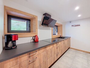 Eine moderne Küche mit Holzausstattung, einer schwarzen Arbeitsplatte, einem roten Wasserkocher, einer Kaffeemaschine und einem Fenster mit Blick auf Grünflächen.