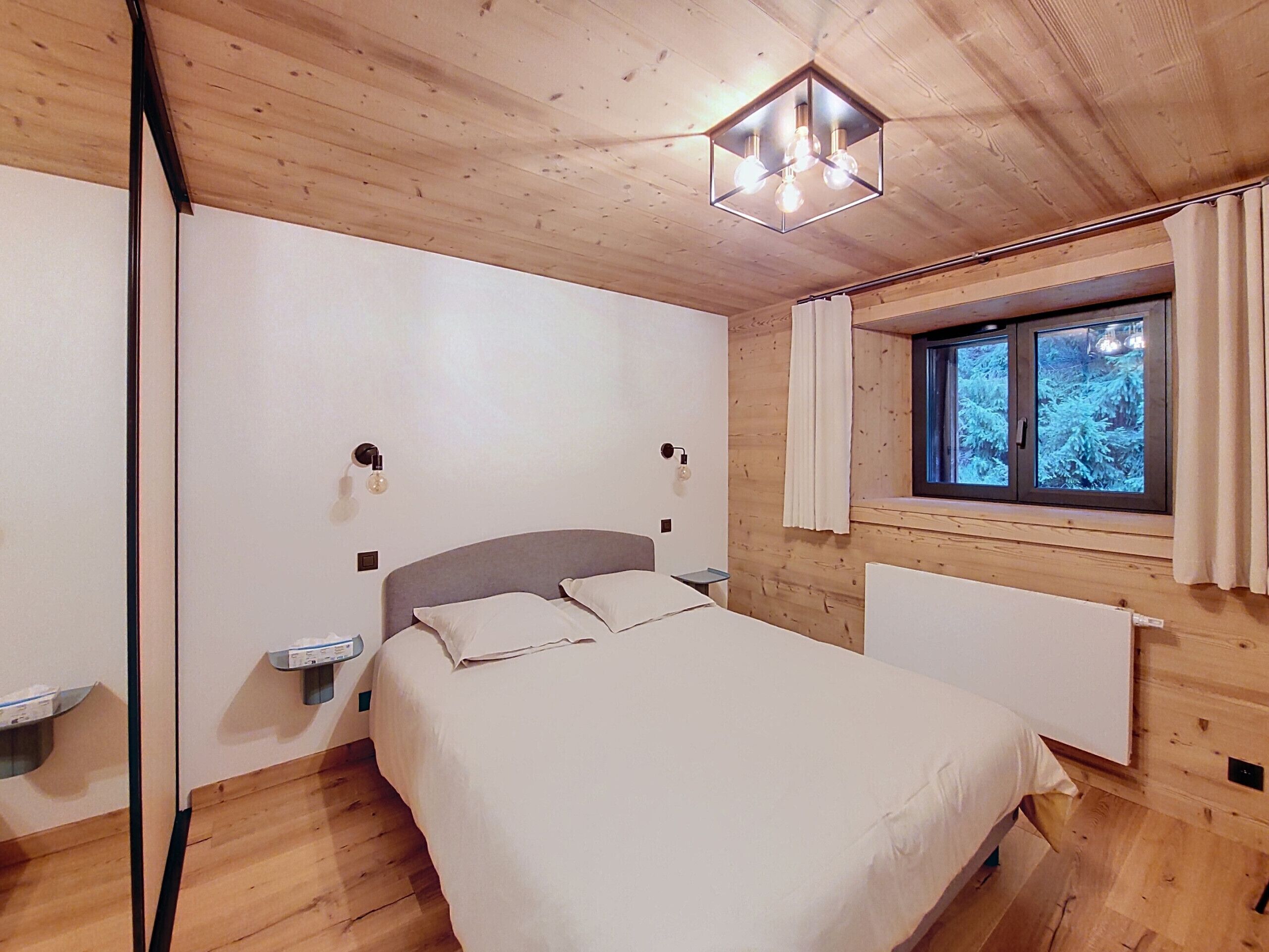A bedroom with a bed, bedside tables, a window with curtains, and a wooden ceiling.